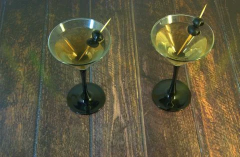 Two full martini glasses with two olives on a toothpick stand on a wooden tab Stock Photos