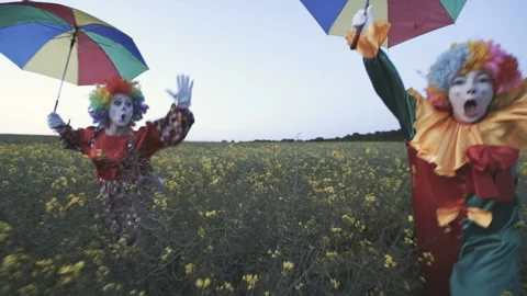 Two funny clowns in colored suits and with colored umbrellas are having fun in Video stock 92181951