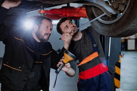 Two funny workers analyze the car underneath, both of which are very Stock Photos