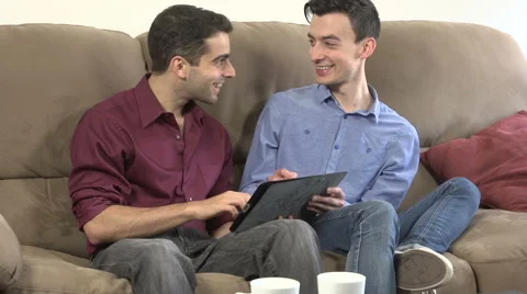 Two gay men, on couch, looking at digital tablet in mid-shot Stock Footage 44110900