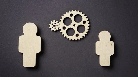 Two gears rotate between two wooden silhouettes of people, stop motion. Stock Footage 121751109