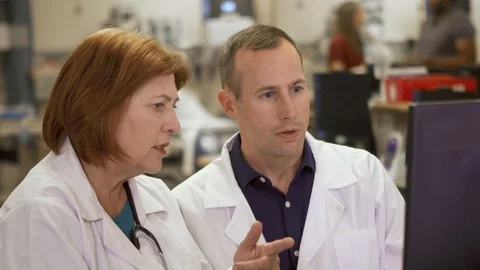 Two generations of doctors consult at a computer to solve a problem in a Stockbeeldmateriaal 119925125