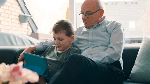Two generations play with a digital tablet at home while sitting in sofa Stock Footage 105128984