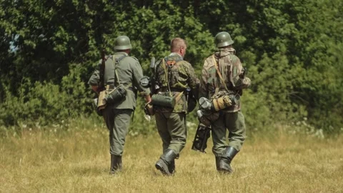 Two German Waffen-SS and one Wehrmacht soldiers walk across open field during Stock Footage 325698427