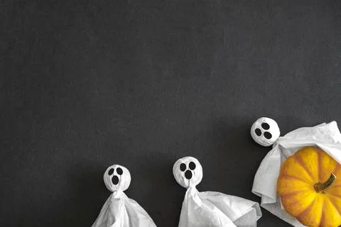 Two ghosts and pumpkin, black background. Top view. Copy space. Stock Photos