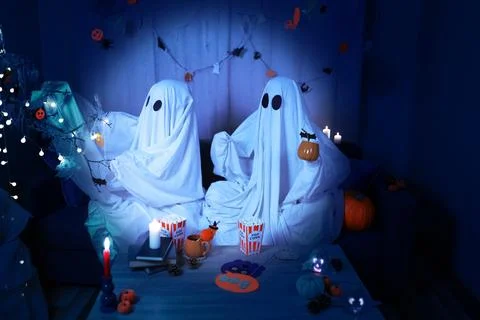Two ghosts in white sheets enjoying Halloween night at home, popcorn, pumpk.. 스톡 사진