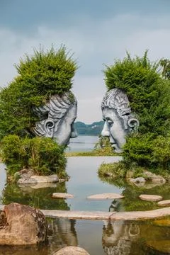 Two Giant Face Sculptures Facing Each Other in a Scenic Lake Park Stock Photos