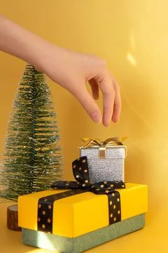 Two gift boxes, Christmas tree and a woman's hand on bright gold background Stock Photos