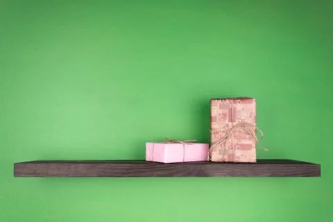 Two gift boxes on a dark color shelf with wood texture mounted on a green wal 库存照片