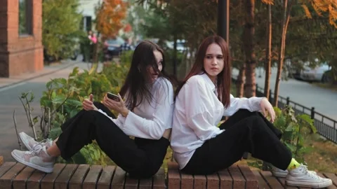 Two girlfriends are arguing, sitting on a street bench apart, young women are in Stock Footage 230985075