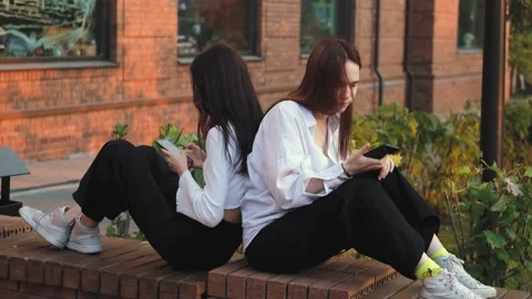 Two girlfriends are arguing, sitting on a street bench apart, young women are in Stock Footage 231044293