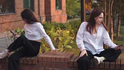 Two girlfriends are arguing, sitting on a street bench apart, young women are in Stock Footage 231331260