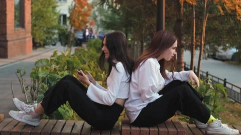 Two girlfriends are arguing, sitting on a street bench apart, young women are in Video stock 231331484