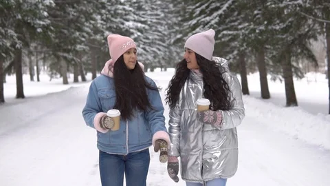 Two girlfriends are walking in the winter forest holding glasses of coffee in Stock Footage 98522997