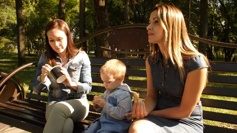 Two girlfriends with a child sit on a bench in the city Park and eat ice cream Stock Footage 94052044