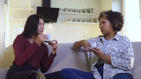 Two girlfriends gossiping while sitting on the couch Stock Footage 172258990