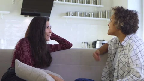 Two girlfriends gossiping while sitting on the couch Stock Footage 179967106