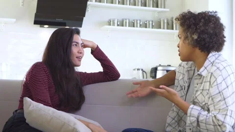 Two girlfriends gossiping while sitting on the couch Stock Footage 179968289