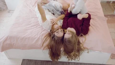 Two girlfriends having fun lying on bed in a cozy room Foto stock