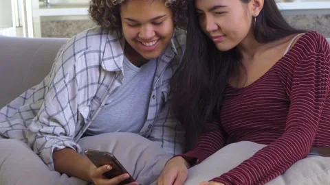 Two girlfriends looking at a smartphone while sitting on the couch Stock Footage 163703709