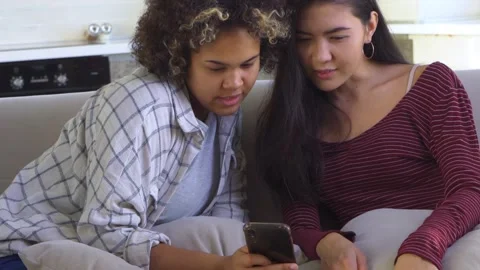 Two girlfriends looking at a smartphone while sitting on the couch Stock Footage 164020235