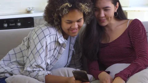 Two girlfriends looking at a smartphone while sitting on the couch Stock Footage 168627450