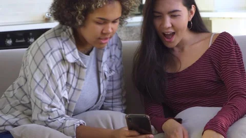 Two girlfriends looking at a smartphone while sitting on the couch Stock Footage 179954870