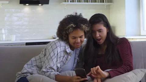 Two girlfriends looking at a smartphone while sitting on the couch Stock Footage 179960638