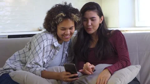 Two girlfriends looking at a smartphone while sitting on the couch Stock Footage 179962650