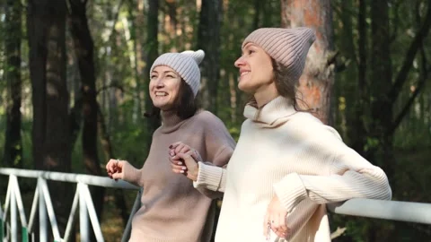 Two girlfriends or sisters in knitted hats are walking outside in an autumn park Stock Footage 270168435
