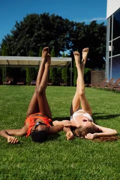 Two girlfriends rest on the grass at pool Stock Photos