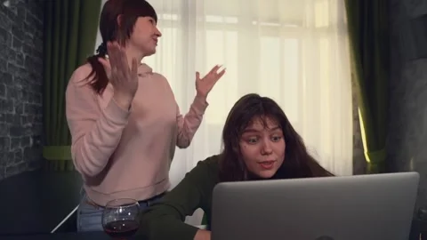 Two girlfriends sitting at laptop begin to rejoice emotionally. Winning Stock Footage 174701041