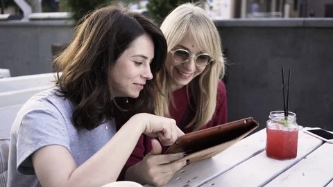Two girlfriends with a tablet in an outdoors cafe 스톡 동영상 84664225
