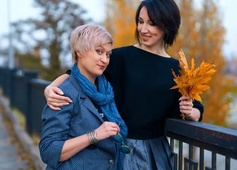 Two girlfriends talking and posing in autumn city park. Beautiful adult woman Stock Photos