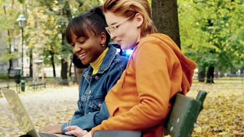 Two girlfriends talking over laptop in autumn park 4K Stock Footage 144565706