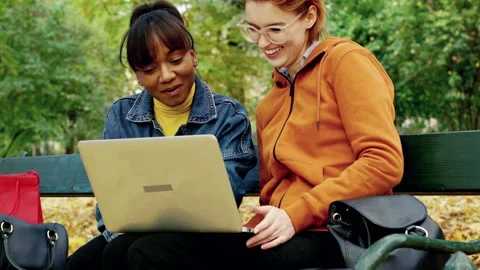 Two girlfriends talking over laptop in autumn park 4K Stock Footage 144566065