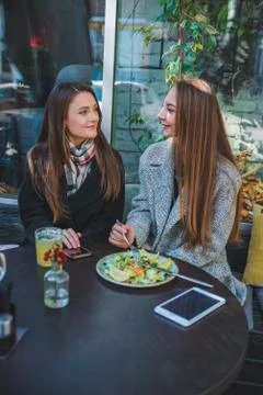 Two girlfriends talking while eating in outdoors cafe autumn time Stock Photos