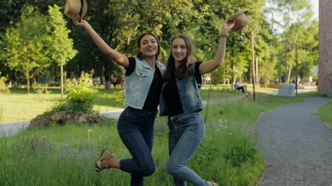 Two girlfriends throw their hats up, having fun outdoors in summer. Video stock 148119104
