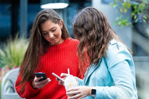 Two girlfriends use a smartphone, laugh and talk, fun together, new normal te Stock Photos