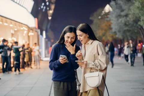 Two girlfriends using their cellphone while exploring a new city at night Stock Photos