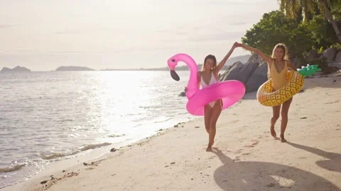 Two girlfriends walk along the beach dancing in the sunset time holding hands Video stock 245449079