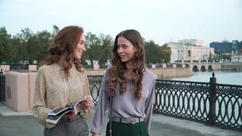 Two girlfriends walk on the bridge flipping through a magazine. 4K Stock Footage 153298773