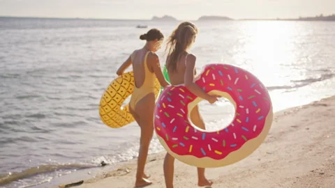 Two girlfriends walking along sunset beach holding hands after swimming in sea Stock Footage 245449262