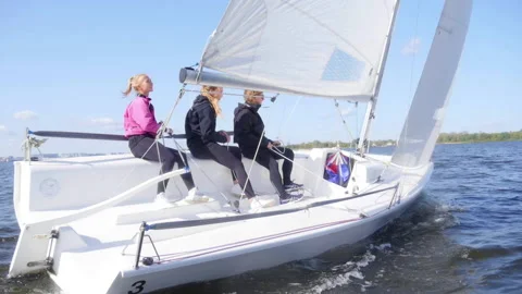 Two girls and a guy manage a small yacht during a river trip in early autumn Stock Footage 143804599