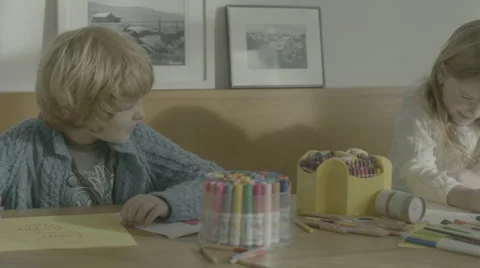 Two girls and one boy sit at a dining room table, drawing and coloring Stock Footage 68348366