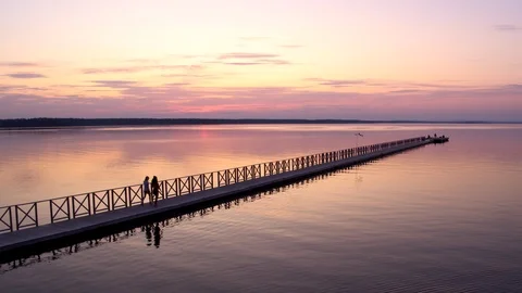 Two girls are walking down the pier in a beautiful sunset and some fishermen at  Stock Footage 116354260