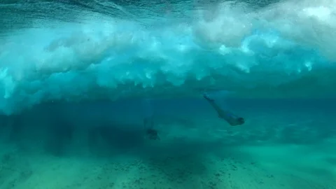 Two girls in bikinis diving under breaking waves 動画素材 127632415