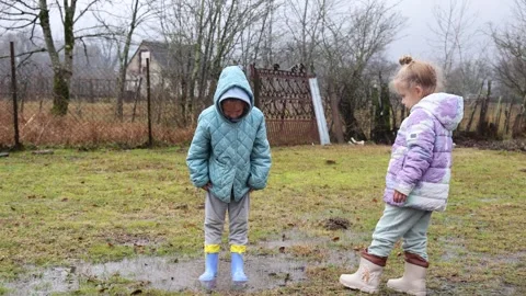 Two girls in boots jump in a puddle in the rain Video stock 308034278