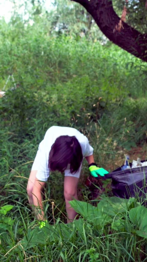 Two girls collecting garbage under big tree near riverbank Stock Footage 340576649