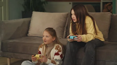Two girls compete in a video game with gamepads, having fun together at home Stock Footage 343423912